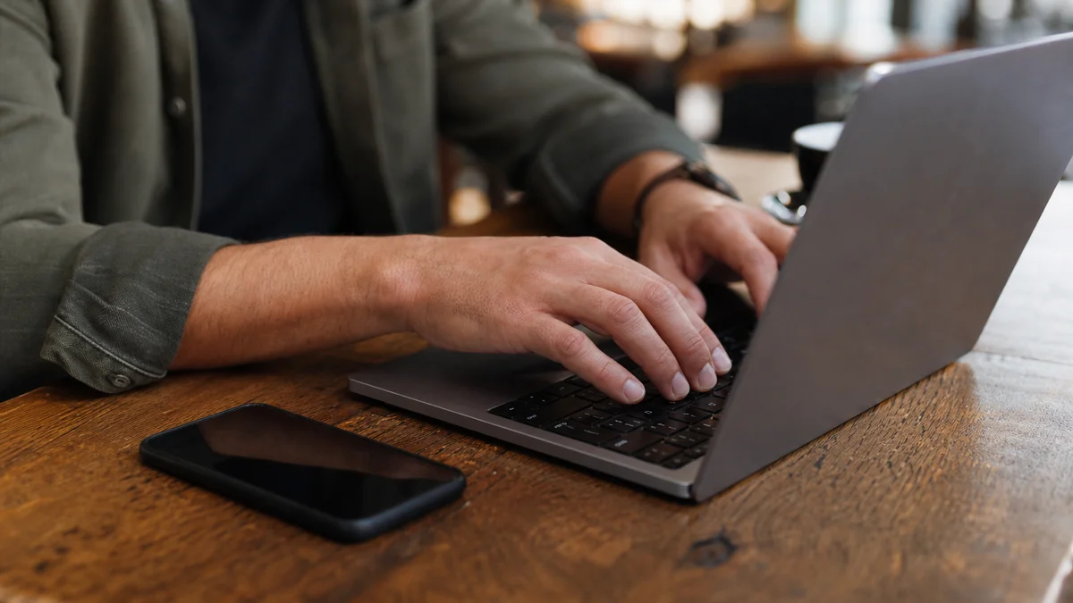 Hands typing on a laptop at a wooden table for Sapling AI Detector review testing