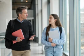 Teacher and student walk through a bright campus corridor discussing what AI checker do teachers use.
